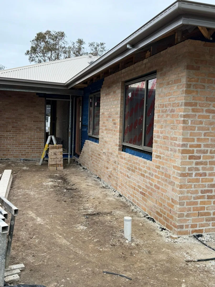Recycled-look face brick partway up the side elevation, with Solitex wall wrap and taped window reveals still visible above