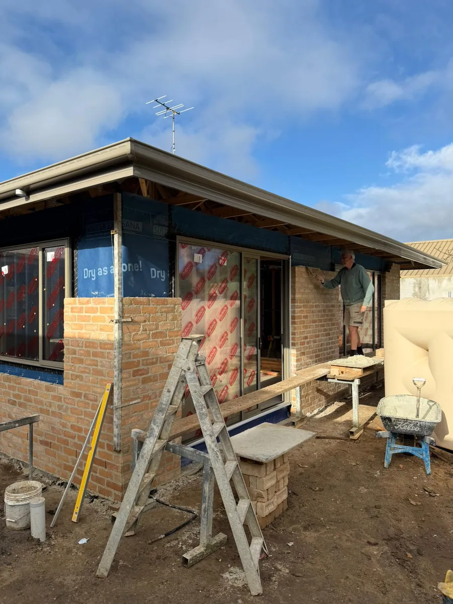 Bricklayer working along the rear of the Moorabbin build, laying brick over the blue Solitex Extrasana wall wrap